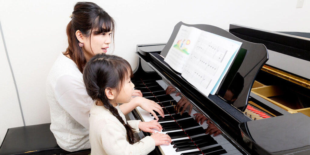 講師が小さなお子様の隣に座って行うピアノレッスンの様子